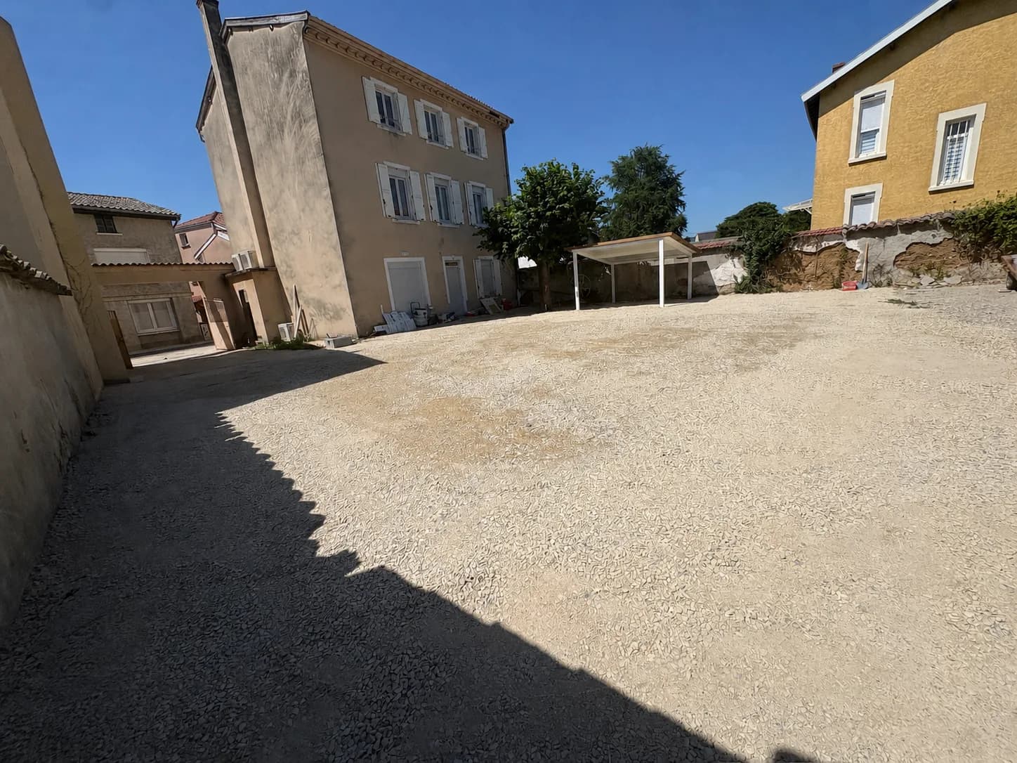 Cour gravillonnée devant le bâtiment de Villa 61 sous un ciel bleu.