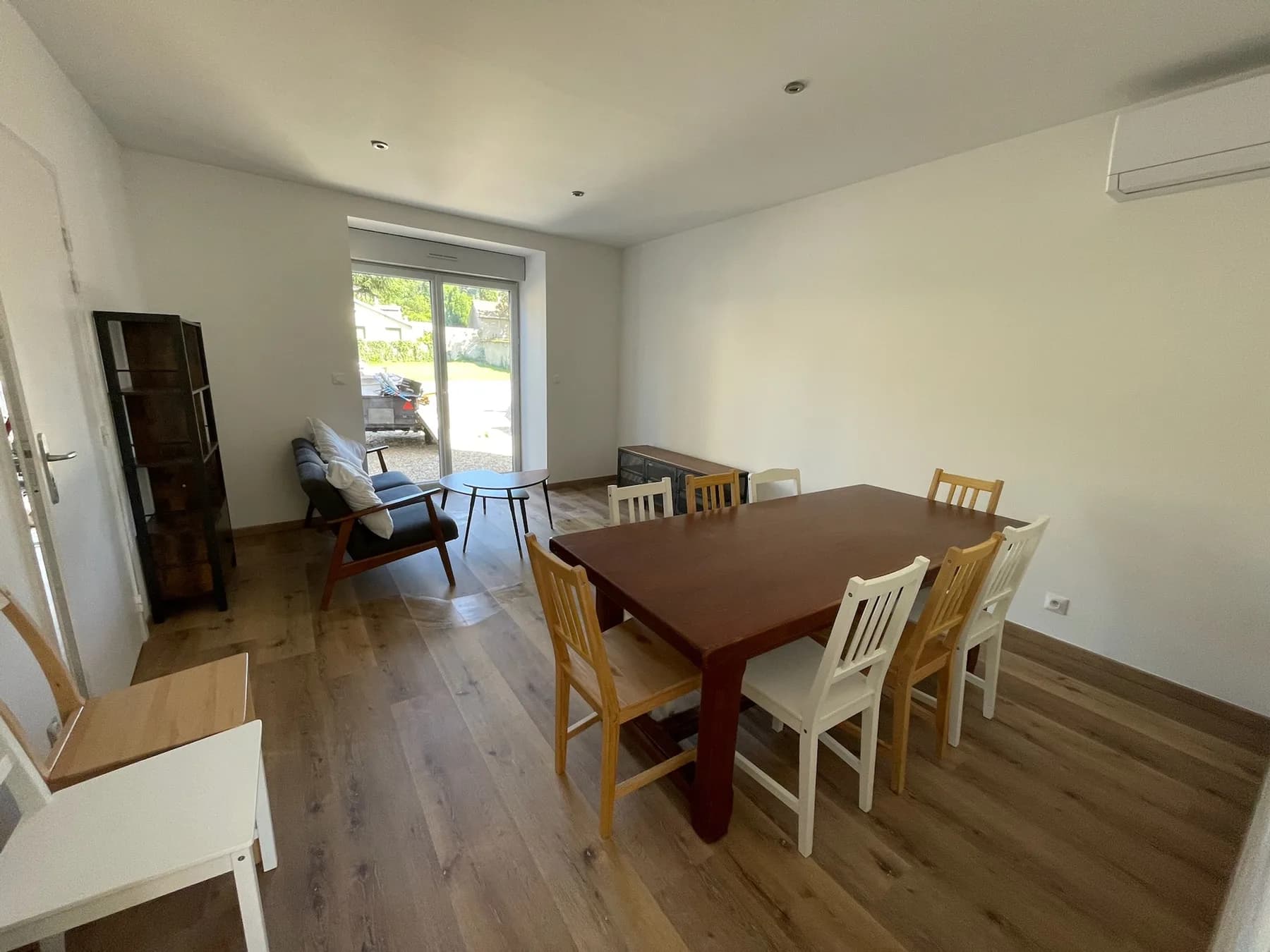 Pièce de vie avec grande table à manger, fauteuils et baie vitrée donnant sur la cour.